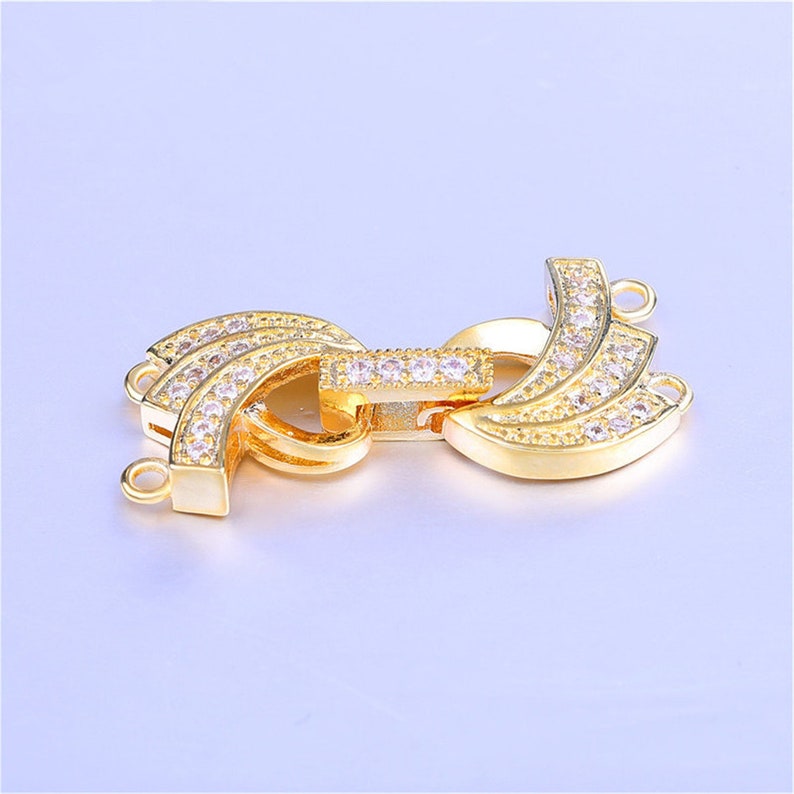 May include: Gold-tone metal clasp with clear crystal accents. The clasp has two loops on each side for attaching jewelry.