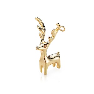 Könnte beinhalten: Ein goldfarbener Hirsch-Anhänger mit einer Schlaufe zum Anbringen an einer Halskette oder einem Armband. Der Hirsch hat ein detailliertes Design mit Geweih und einem kleinen Auge.