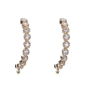May include: A pair of gold hoop earrings with a row of clear cubic zirconia stones around the hoop.