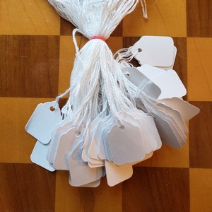 May include: A bundle of white string with white square tags attached. The tags have a hole punched in the top corner.