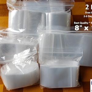 May include: A large stack of clear plastic resealable bags with a zipper closure. The bags are 2 mil thick and measure 8 inches by 10 inches. The text on the bags reads "2 Mil", "Free Shipping", "2-3 Day Delivery", "Best Quality ~ Best Deal", and "8" x 10".