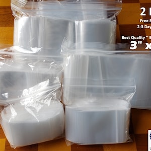 May include: A large quantity of clear plastic resealable bags, 2 mil thick, 3 inches by 4 inches, with a zipper closure. The bags are stacked and arranged on a checkered surface. The text "2 Mil", "Free Shipping", "2-3 Day Delivery", "Best Quality ~ Best Deal", "3" x 4"" is printed on a white label.