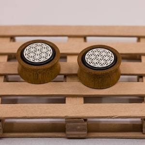 May include: A pair of wooden ear gauges with a black and white flower of life design. The gauges are on a wooden pallet.