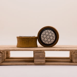 May include: Two wooden ear gauges, one with a black and white geometric design and the other plain, on a wooden pallet.