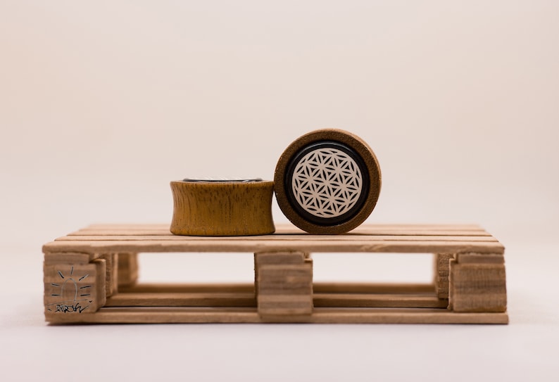 May include: Two wooden ear gauges, one with a black and white geometric design and the other plain, on a wooden pallet.