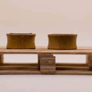 May include: Two wooden ear gauges, one on each side of a small wooden pallet. The gauges are a light brown color and have a smooth finish.