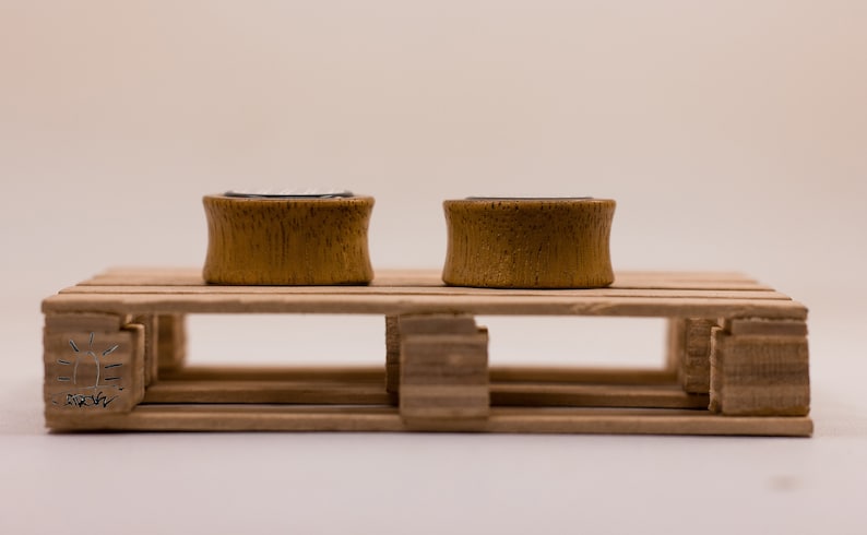 May include: Two wooden ear gauges, one on each side of a small wooden pallet. The gauges are a light brown color and have a smooth finish.