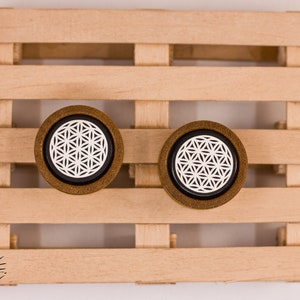 May include: Two wooden ear gauges with a black background and a white flower of life design.