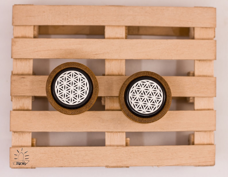 May include: Two wooden ear gauges with a black background and a white flower of life design.