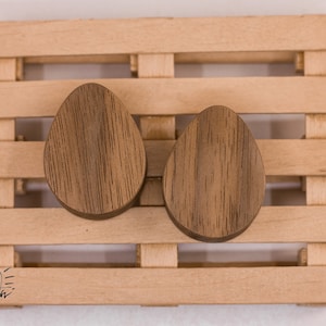 Puede incluir: Dos tapones para orejas de madera marrón, cada uno con un patrón único de veta de madera, se muestran en una paleta de madera.