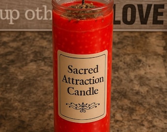 May include: A red candle with a label that reads "Sacred Attraction Candle". The candle is lit and has a small amount of herbs on top.