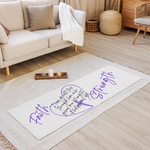 Puede incluir: Esterilla de yoga blanca con escritura morada que dice "Fe" y "Fuerza". La esterilla también presenta un diseño en forma de corazón con el texto "Todo lo puedo en Cristo que me fortalece - Filipenses 4:13".