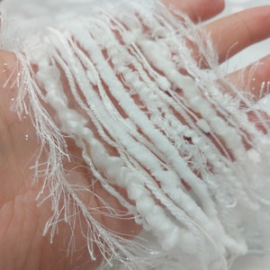 May include: White yarn with a fluffy, textured appearance. The yarn is arranged in a loose, flowing pattern, creating a soft and delicate look.