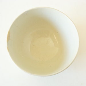 May include: A white ceramic bowl with a slightly off-white interior. The bowl is empty and has a smooth, glossy finish.
