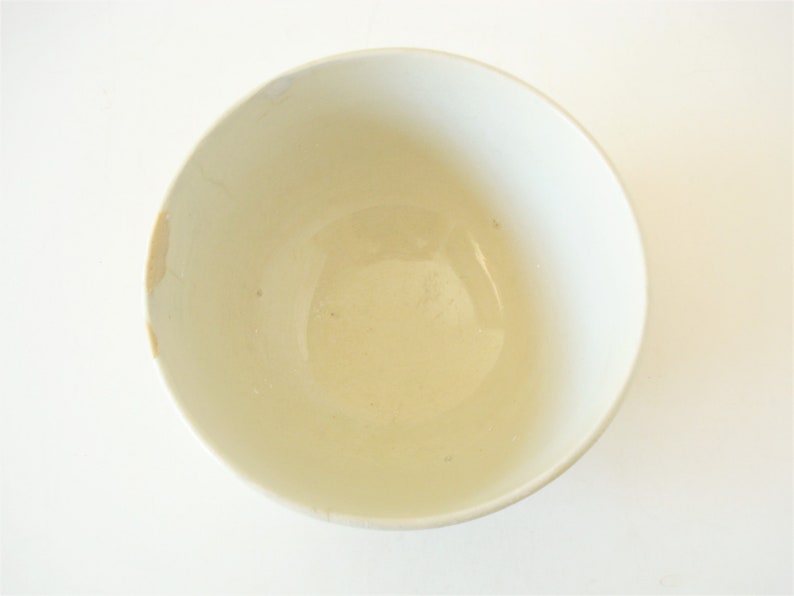 May include: A white ceramic bowl with a slightly off-white interior. The bowl is empty and has a smooth, glossy finish.