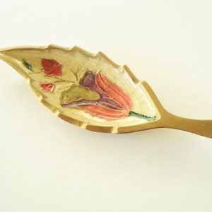 Könnte beinhalten: Eine Schale aus Messing in Blattform mit einem floralen Design in Rot-, Rosa-, Grün- und Violetttönen.