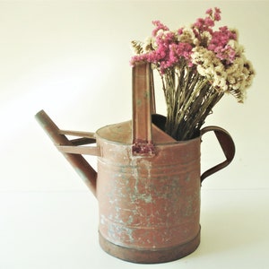 May include: A vintage, rusty metal watering can with a handle and spout, filled with a bouquet of dried pink and white flowers.