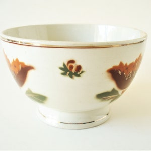 May include: A white ceramic bowl with a gold rim and brown and green floral designs.