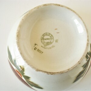 May include: The bottom of a white ceramic bowl with a green and brown floral design. The bowl has a green and gold label that reads "Villa Nova, Frenchen, Portugal".