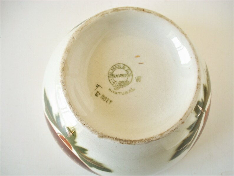 May include: The bottom of a white ceramic bowl with a green and brown floral design. The bowl has a green and gold label that reads "Villa Nova, Frenchen, Portugal".