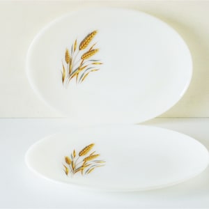 May include: Two white oval serving platters featuring a wheat design. The platters are made of ceramic and have a glossy finish. The wheat design is in shades of gold and brown.