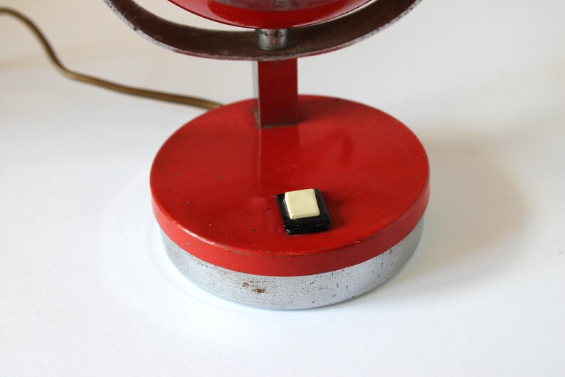 May include: A vintage red and silver desk lamp with a circular base and a push button switch. The lamp has a red shade and a silver metal frame. The lamp's base is approximately 4 inches in diameter.