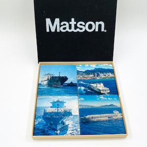 May include: A set of four coasters featuring images of ships and the city skyline. The coasters are in a box with the word "Matson" printed on the top.