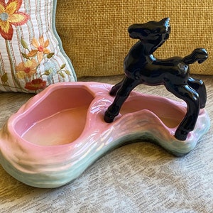 Op de afbeelding: Een roze en blauwe keramische schaal met een zwart keramiek paardenbeeld erop. De schaal heeft een golvend ontwerp en twee compartimenten.