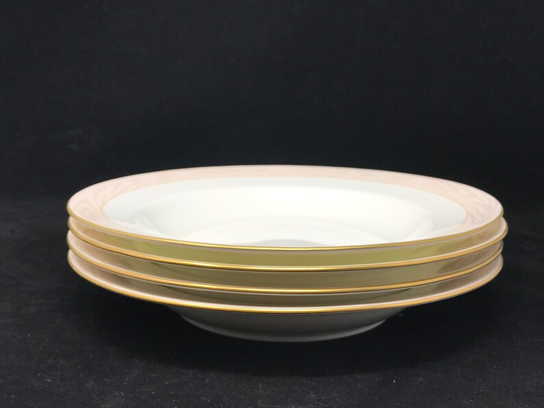 May include: Three white soup bowls with a gold rim and a pale pink band. The bowls are stacked on top of each other.