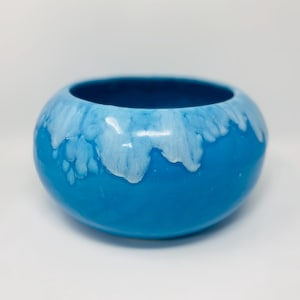 May include: A round, ceramic bowl with a glossy finish. The bowl is a vibrant blue color, with a lighter, white-blue glaze dripping down from the rim. The interior of the bowl is a darker shade of blue.