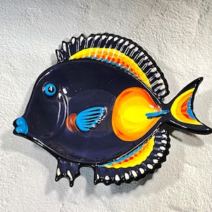 May include: A ceramic fish-shaped dish featuring a dark navy blue body with a bright yellow circular patch near the tail. The fins are accented with vibrant yellow, orange, and light blue stripes, while the eye is a solid light blue circle.