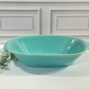 May include: An oval-shaped turquoise serving bowl with integrated side handles. The bowl features a smooth, glossy finish and a deep basin, providing a wide opening for serving food. The design is simple, functional, and uniform in color.