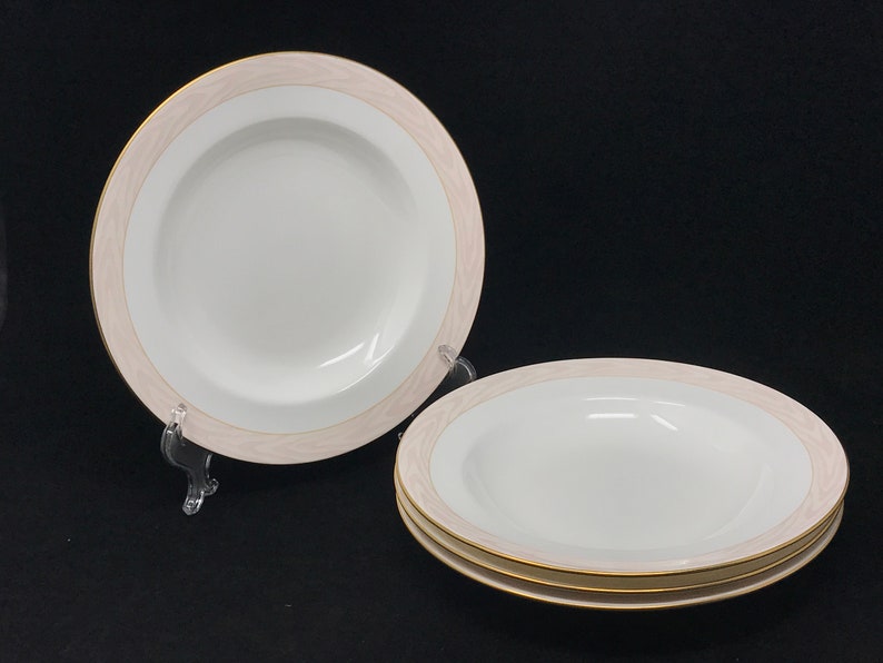 May include: Three white ceramic soup bowls with a pink and gold rim. The bowls are stacked on top of each other.