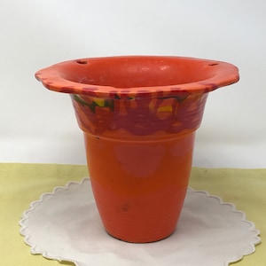 Peut inclure: Pot en céramique orange avec un bord festonné et un motif peint de tourbillons rouges, orange et verts. Le pot a trois trous de drainage.