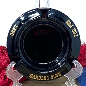 Puede incluir: Cenicero de cerámica negro con letras doradas que dicen "Harold's Club", "For Fun" y "Reno".