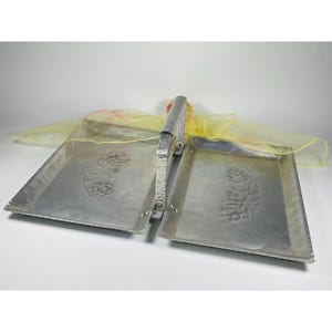 May include: A silver serving tray with a handle and two sections. Each section has an embossed floral design. The tray is sitting on a yellow sheer fabric.