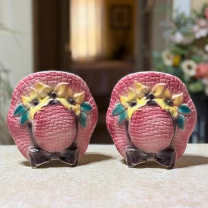 Peut inclure: Une paire de salières et poivrières en céramique en forme de chapeaux de soleil tressés roses. Chaque chapeau présente un bouquet de fleurs jaunes avec des feuilles vertes au centre et un nœud brun foncé à la base, avec une finition brillante.