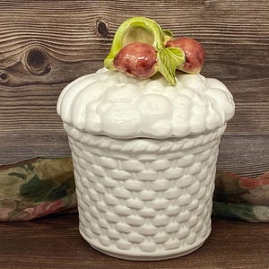 May include: White ceramic canister with a basket weave design and a lid decorated with a cluster of red and green fruit.