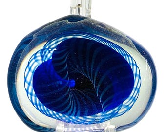 Könnte beinhalten: Ein blau-weißes Kunstglas-Briefbeschwerer mit einem wirbelnden, augenartigen Design. Das Innere zeigt einen tiefblauen Wirbel, umgeben von konzentrischen Ringen aus Weiß und Blau. Das Glas ist auf einem transparenten Acrylständer montiert.