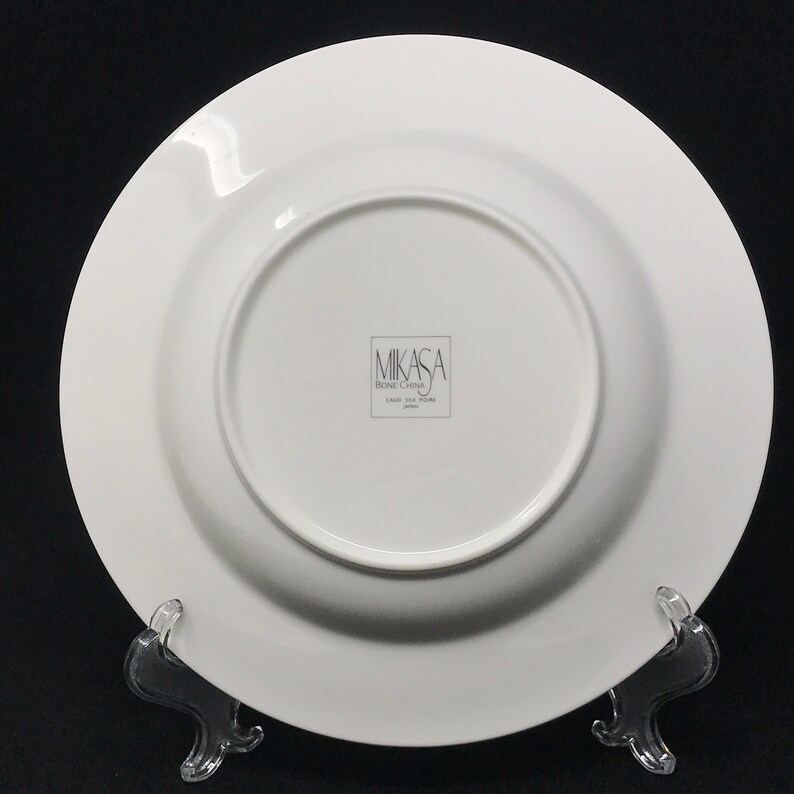 May include: White Mikasa bone china dinner plate with a raised rim. The plate has the words "Mikasa Bone China" printed on the bottom.