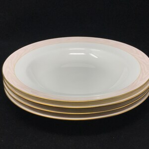 May include: Three white ceramic soup bowls with a pink and gold rim. The bowls are stacked on top of each other.