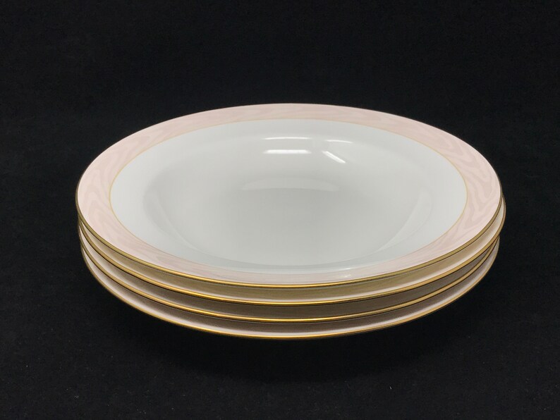 May include: Three white ceramic soup bowls with a pink and gold rim. The bowls are stacked on top of each other.