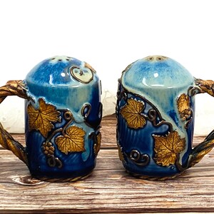 May include: A pair of blue and gold ceramic salt and pepper shakers with a vine design and twisted handles.