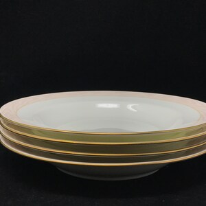 May include: Three white soup bowls with a gold rim and a pink band around the edge. The bowls are stacked on top of each other.
