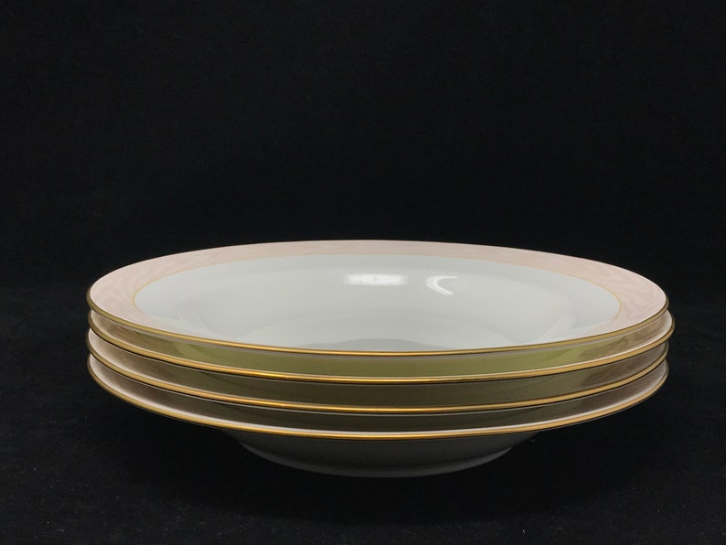 May include: Three white soup bowls with a gold rim and a pink band around the edge. The bowls are stacked on top of each other.