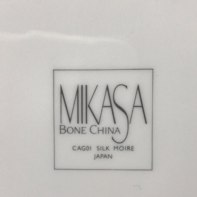May include: A white Mikasa bone china plate with the text "Mikasa Bone China CAGO1 Silk Moire Japan" printed on the bottom.