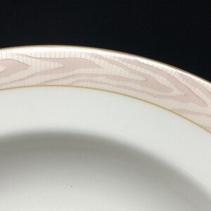 May include: Close-up of the rim of a white ceramic bowl with a pink and gold woodgrain design.