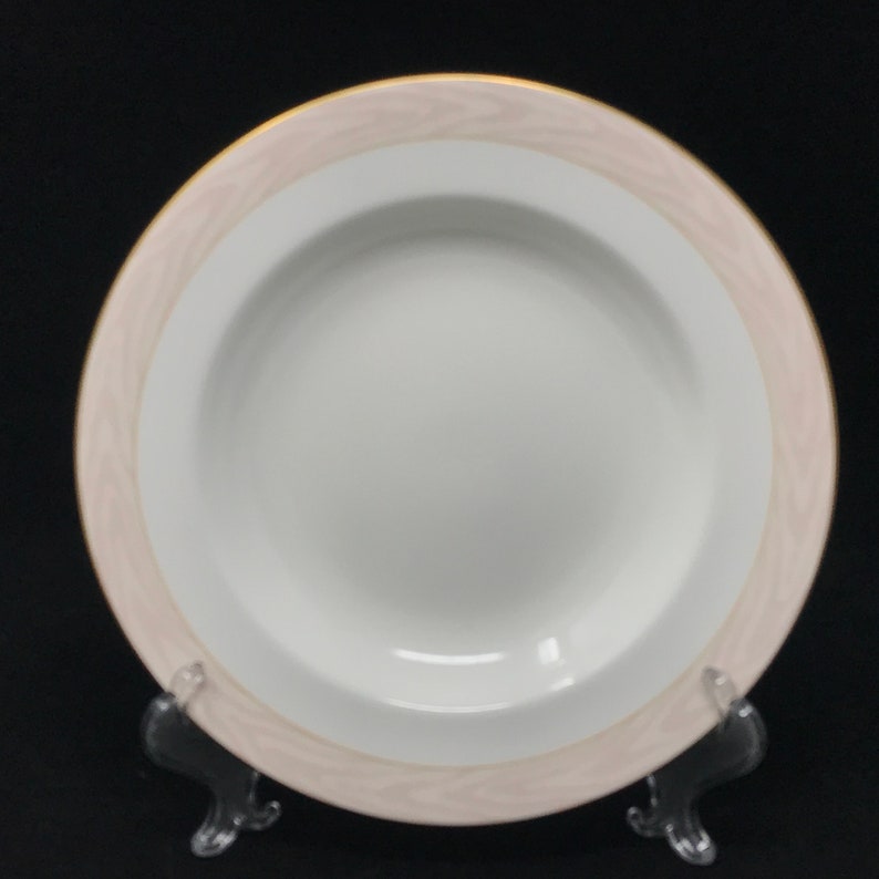 May include: A white porcelain soup bowl with a wide, shallow rim. The bowl has a pink and gold decorative border.