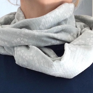 Könnte beinhalten: Ein weißer Schal mit einem zarten Blumenmuster. Der Schal ist aus einem weichen, leichten Stoff gefertigt und perfekt zum Schichten in den kühleren Monaten.