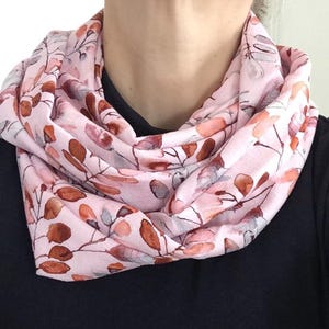 Könnte beinhalten: Ein rosa Infinity-Schal mit einem Blättermuster im Aquarellstil in Braun-, Orange- und Grautönen. Der Schal ist um den Hals gelegt und zeigt den weichen, fließenden Stoff und das zarte botanische Design.